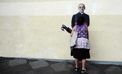 Una mujer besa un mural de Romero pintado sobre una pared de San Salvador